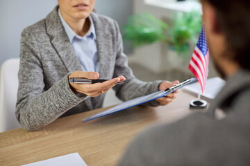 US visa interview at consulate, officer reviewing applicant documents at office desk with United...