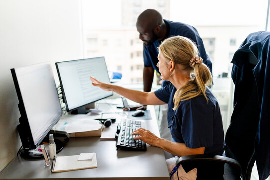 Senior female doctor discussing medical records on computer with male colleague in office