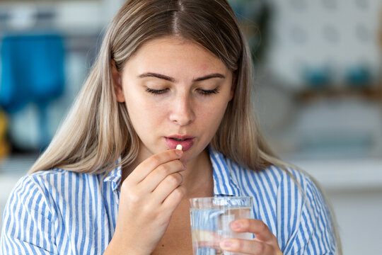Woman taking medicine pill with water. Healthcare and medicine concept. Attractive young female holding a yellow capsule and glass of water. Medical treatment, pharmacy and health care at home.