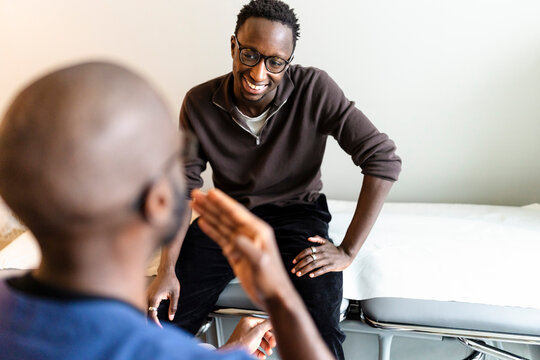 High angle view of young man understanding sign language of male doctor while sitting on examination table
