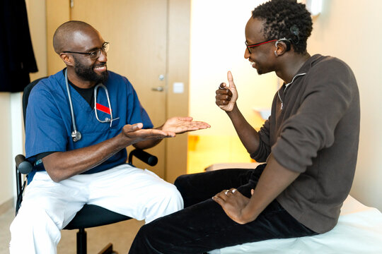 Smiling male doctor and patient communicating in sign language with each other at hospital examination room