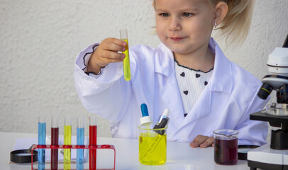 Little girl scientist looking at yellow liquid in a test tube during experiment