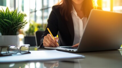 Young woman sitting on desktop laptop holding pencil writing notepad in office indoors