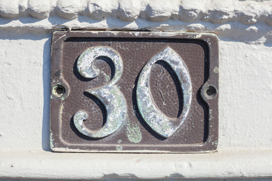 Altes, verziertes Hausnummernschild Nr. 30 auf weisser Hauswand, Deutschland