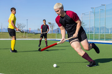 White male athlete sprinting and controlling ball with hockey stick on synthetic turf
