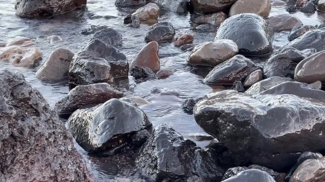 Calm ocean waves washing a rocky shore at dawn, soft pastel blue light before sunrise, minimal coastal scenery conveying freedom, travel lifestyle, nature balance, environment and relaxing seaside mor