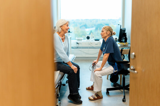 Senior female physician talking with patient sitting on examination table in clinic
