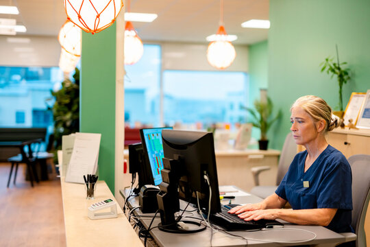Concentrated senior female hospital receptionist working on computer at desk