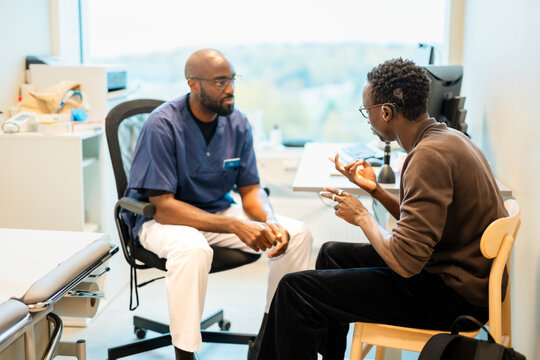 Young man communicating through sign language with male doctor while sitting in hospital room