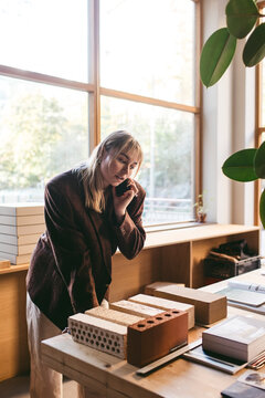 Female design professional talking on smart phone while looking at bricks kept on table in office