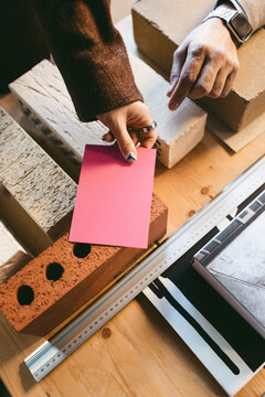 High angle view of female designer's hand holding paper on brick while showing design process in office