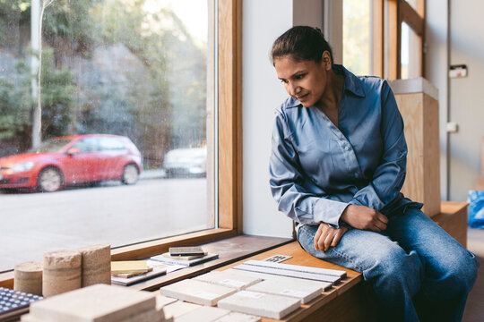 Mature female architect examining artifacts while sitting near window in new office