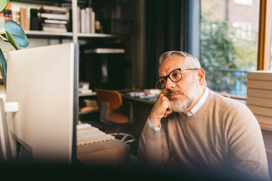 Bored mature businessman leaning on elbow while looking at computer in office