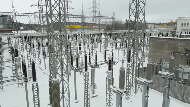 Detailed aerial view of a high voltage substation blanketed in fresh snow, showing insulated structures and grid components during extreme cold conditions.
