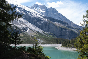 Obraz premium Turquoise alpine lake framed by conifer forest and snow-capped peaks - Oeschinensee, Kandersteg, Bern, Switzerland