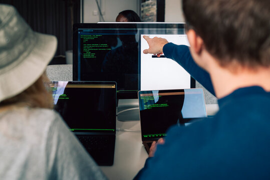 Rear view of male and female programmers discussing with each other on desktop PC in office