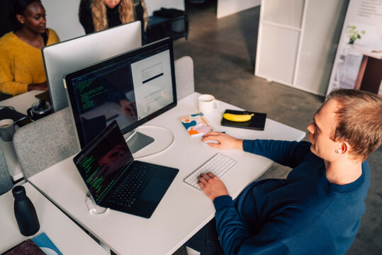 High angle view of male tech expert working on computer while sitting at desk in startup office