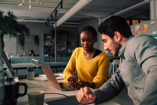Male business expert sitting with female colleague using laptop while working in tech office