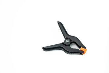Obraz premium Black plastic spring clamp isolated on white background. Adjustable hand tool for fixing materials in woodworking, photography studio, DIY projects and workshop use.
