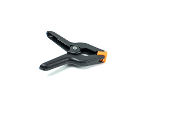 Obraz premium Black plastic spring clamp in open position isolated on white background. Adjustable hand clamp tool for woodworking, photography studio, DIY projects and workshop use.
