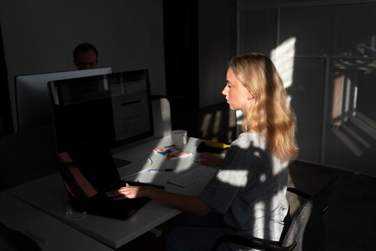 Blond female tech expert working at desk in dark office