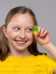 smiling girl in a close-up shot against a light neutral background. She has fair skin and light brown hair styled in two low pigtails. She is wearing a bright yellow knitted T-shirt that matches well 