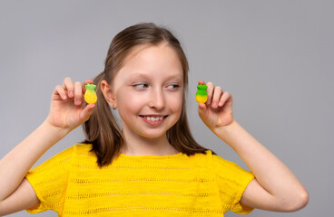 smiling girl in a close-up shot against a light neutral background. She has fair skin and light brown hair styled in two low pigtails. She is wearing a bright yellow knitted T-shirt that matches well 