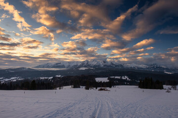 Scenic winter landscape of the Tatra Mountains at dawn. Snow-covered peaks and frosty pine forests under a crisp blue morning sky.