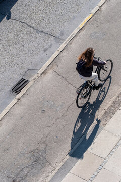 Aerial view of cyclist on bicycle crosses street casting shadow as urban commute turns to motion over pavement in calm quiet solitude