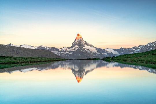 View of the iconic Matterhorn's peak ablaze with golden light, mirrored in the tranquil Stellisee lake under a serene sky, a picturesque alpine scene, Zermatt, Valais, Switzerland.