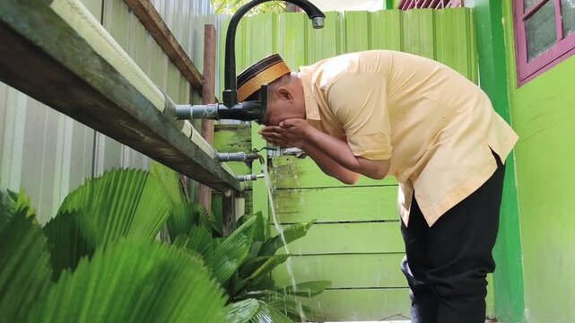 Footage showing a Muslim man performing wudu by rinsing his mouth with clean water before prayer. The scene takes place at a mosque or ablution area