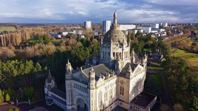 Drone pulls back in arc revealing sunlit Lisieux Basilica and city in Normandy
