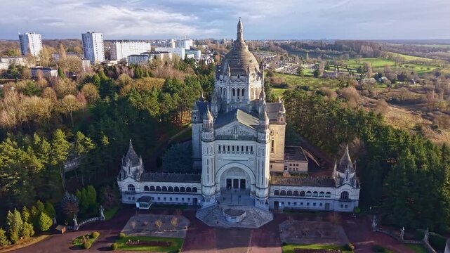 Smooth drone panning revealing sunlit Basilica Sainte-Th&eacute;r&egrave;se with forest backdrop