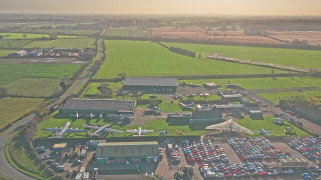 Newark Air Museum in Nottinghamshire, United Kingdom, revealing Avro Vulcan B.2, Victor and Nimrod aircraft displayed outdoors among hangars, runway, drone pulling out revealing surrounding rural area