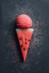 Pink watermelon ice cream cone with colorful sprinkles on dark stone background