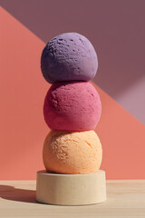 Three stacked sorbet scoops in pink, orange and purple on neutral background