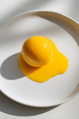 Single mango ice cream sphere melting on white plate in bright natural light