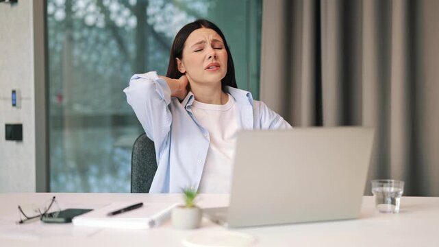 Woman experiences sudden, intense neck pain working on laptop, expressing discomfort and frustration. Seeks relief by massaging sore neck muscles, clear signs of strain from prolonged computer use.