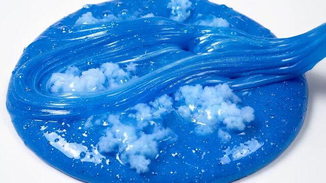 A hand interacts with a bright blue slime, creating waves in the glossy texture. The blue slime is embedded with fluffy white clouds, showcasing playful elements within the slime.