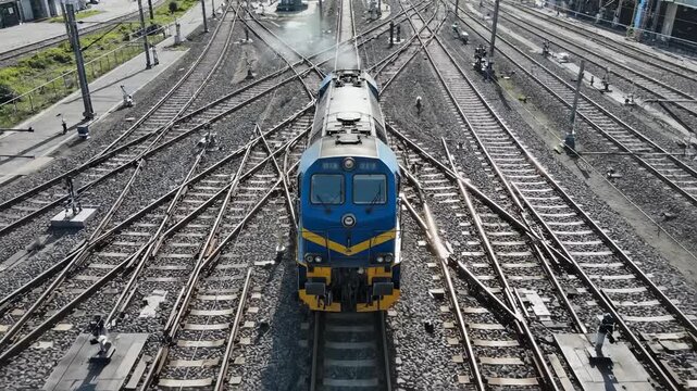 A blue and yellow train is positioned on a complex track layout. Surrounding tracks create a busy scene with numerous junctions and signals near the train.
