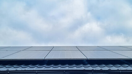 Solar panels installed on tiled residential rooftop under cloudy sky. Renewable energy and sustainable technology concept. Minimal composition with copy space © Natalia_SL