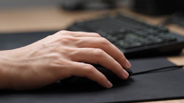 Close up shot of hand using black computer mouse on mousepad with keyboard in background for gaming and office