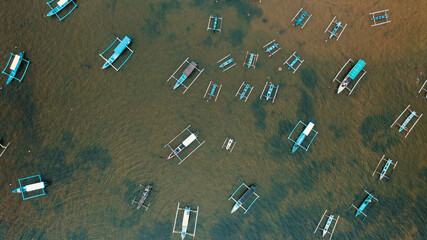 Top-down drone aerial view of traditional Balinese outrigger boats anchored in shallow sea near Sanur, Bali, Indonesia. © NTG Drone Media