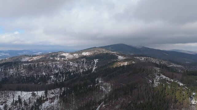 Winter mountain landscape seen from above with sunlit snowfields and dense clouds moving low across frozen ridges and valleys.