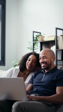 Video of happy beautiful couple using computer while sitting on the couch at home.