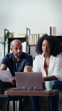Video of couple using their laptop to consulting some invoices and documents while sitting on the couch at home.