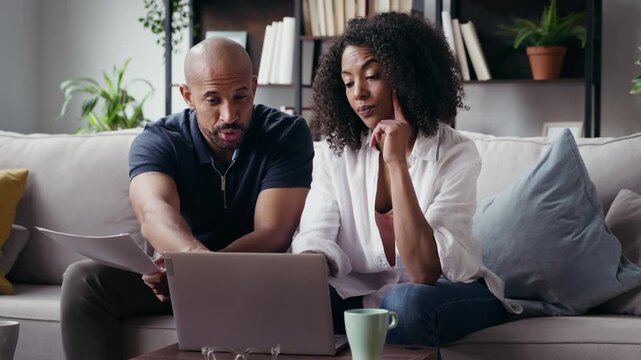Video of couple using their laptop to consulting some invoices and documents while sitting on the couch at home.