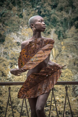 A dark-skinned woman stands in the tropical jungle, covering herself with two large plant leaves. The scene blends natural aesthetics with fashion &mdash; a harmony between human and nature, freshness of tr