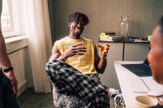 Happy male tech professional discussing with colleagues while sitting on chair in office