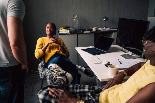 Female tech expert talking with colleagues while sitting at desk in startup office